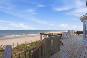 Eine Holzterrasse mit Blick auf den Strand, einem Geländer und Liegestühlen.