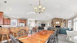 A spacious kitchen with a large island, a dining area with a wooden table, and a living room with a fireplace. - Oceanfront home with direct beach access, community pool & private hot tub (North Topsail Beach)