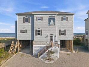 Une propriété de deux étages située en bord de mer, dotée d’une allée couverte menant à l’entrée, d’un petit jardin et offrant une vue sur l’océan.