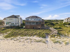 A beachfront property with multiple-story houses, a wooden deck, and a sandy beach area.