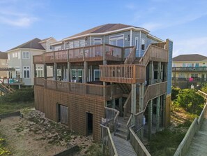 Une maison de plusieurs niveaux située en bord de mer, dotée d’une terrasse en bois et d’escaliers.