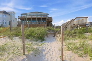 Une propriété située en bord de mer, avec une passerelle en bois menant à une maison dotée de plusieurs balcons.