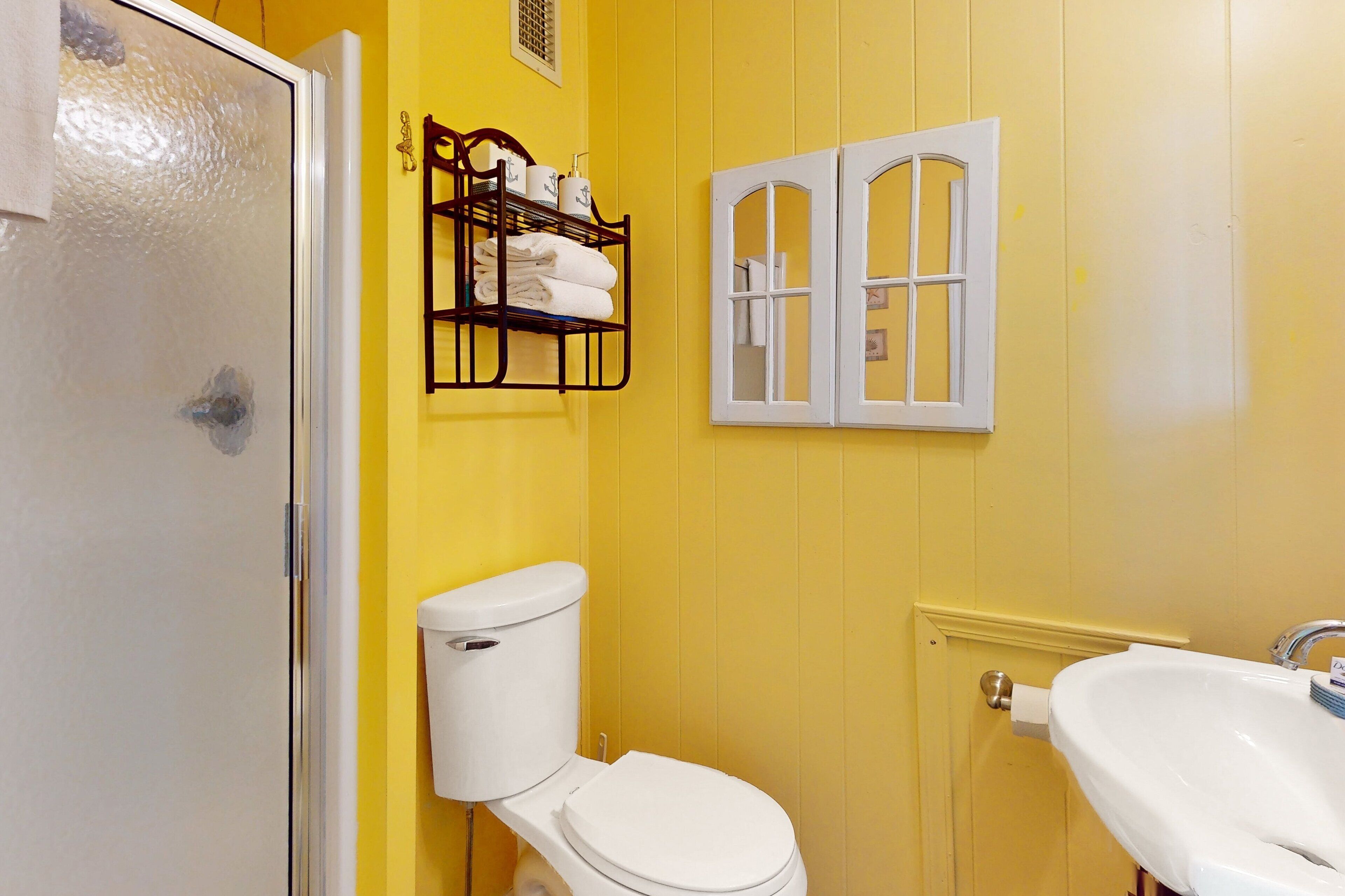 Une salle de bain avec des murs jaunes, des toilettes blanches, un lavabo blanc et un porte-serviettes avec des serviettes pliées.