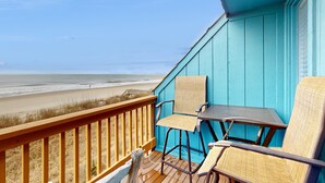A balcony with a view of the beach, featuring two chairs and a small table.