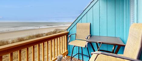 A balcony with a view of the beach, featuring two chairs and a small table.