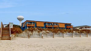 A beachfront hotel with a distinctive blue and orange facade, a water tower, and a wooden staircase leading to the entrance.