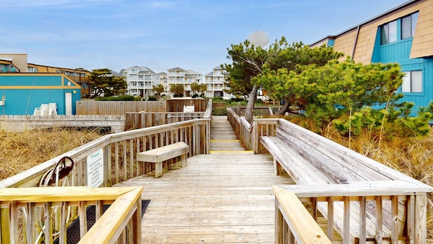 A wooden boardwalk leading to a building with multiple balconies and a clear sky.