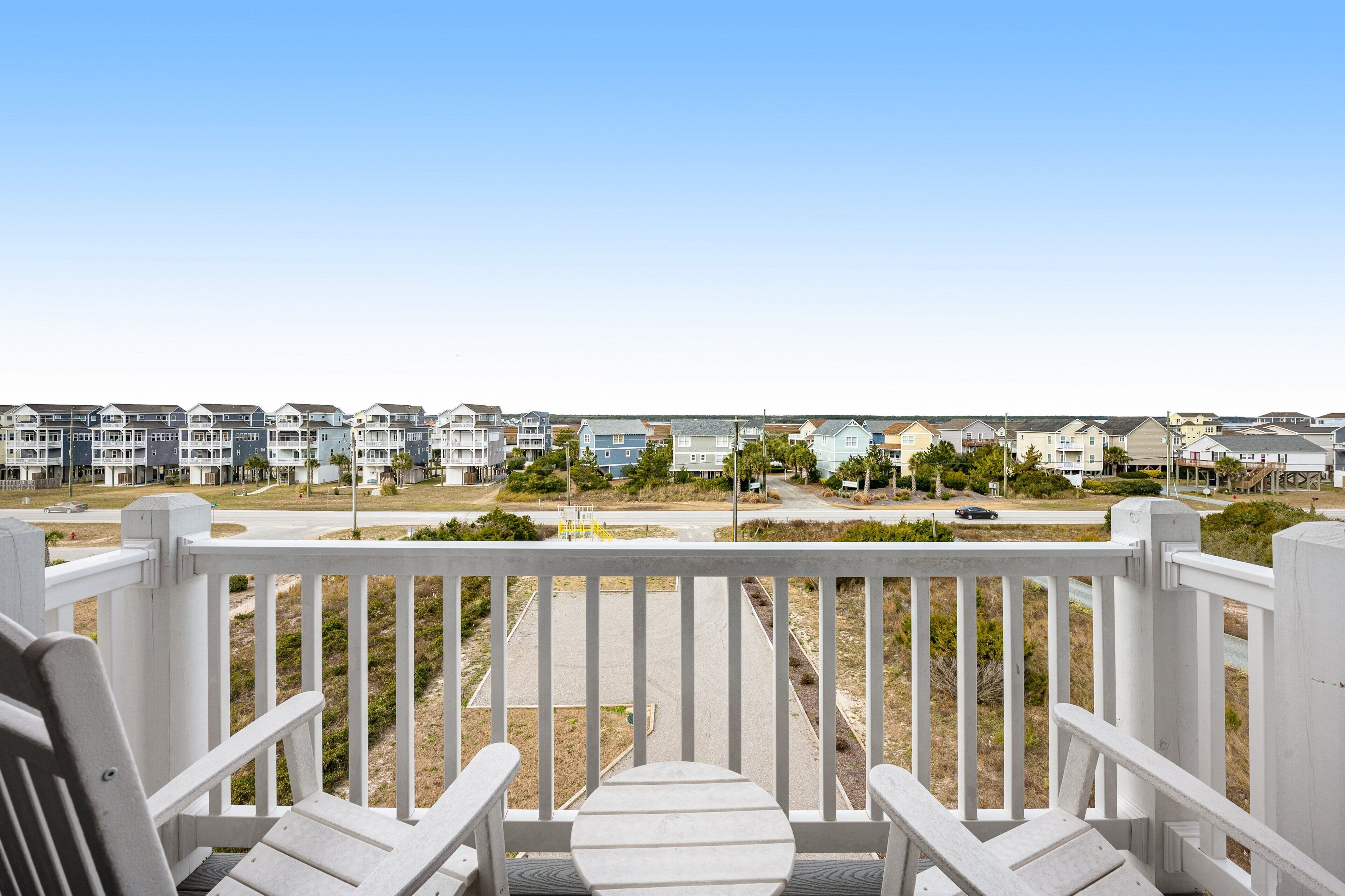 A balcony with white railings and two Adirondack chairs.