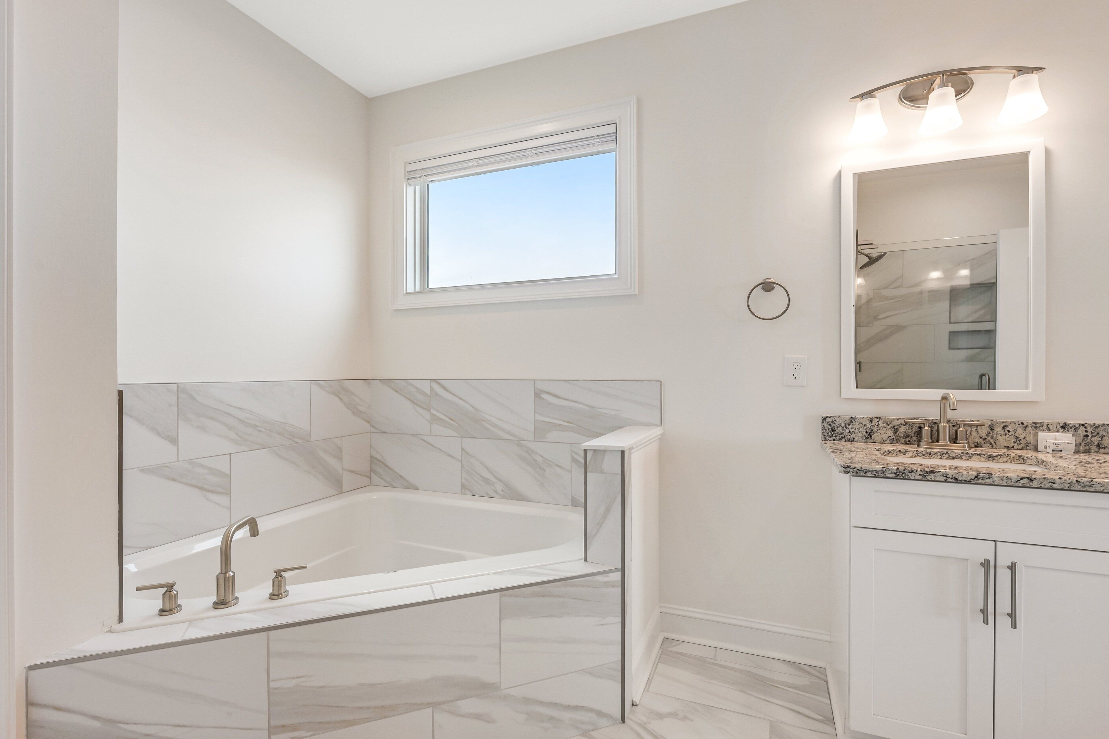 A modern bathroom with a marble-tiled wall, a freestanding bathtub, and a vanity with a granite countertop.