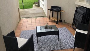 Une terrasse avec une table et des chaises, un barbecue et une vue sur une maison et des collines.