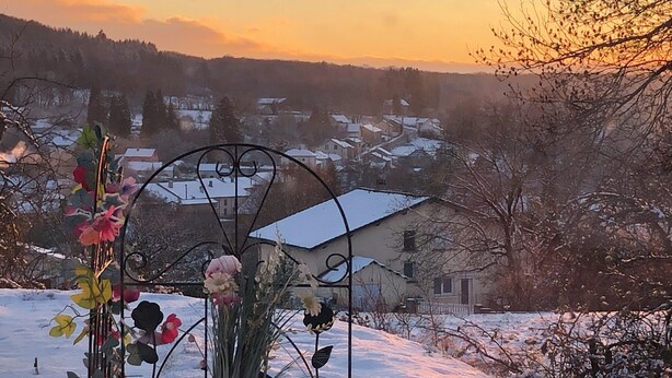 Un paysage enneigé avec une composition florale en métal au premier plan et des maisons en arrière-plan.