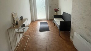 Un couloir doté d’un parquet en chevrons, une porte avec un panneau en verre dépoli, un paillasson noir, une console blanche ornée d’objets décoratifs et un canapé noir.