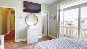 Un dormitorio con una cama grande, televisor montado en la pared, cómoda y balcón con vistas.