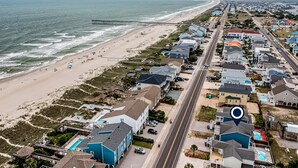 Vista aérea de una zona residencial costera con propiedades frente al mar, un muelle y una carretera que discurre paralela a la playa.