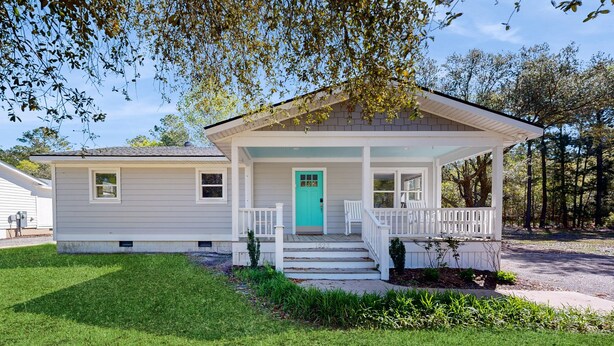 Una casa a un piano con portico, una porta color turchese e un piccolo giardino antistante.