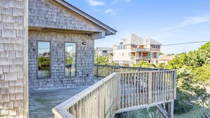 A wooden deck with a railing, a clear sky, and a residential building in the background. - Handsome raised home with private hot tub, & central AC (Waves)
