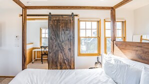 A bedroom with a bed, a desk, and a chair. There is a large window and a sliding door. - Handsome raised home with private hot tub, & central AC (Waves)