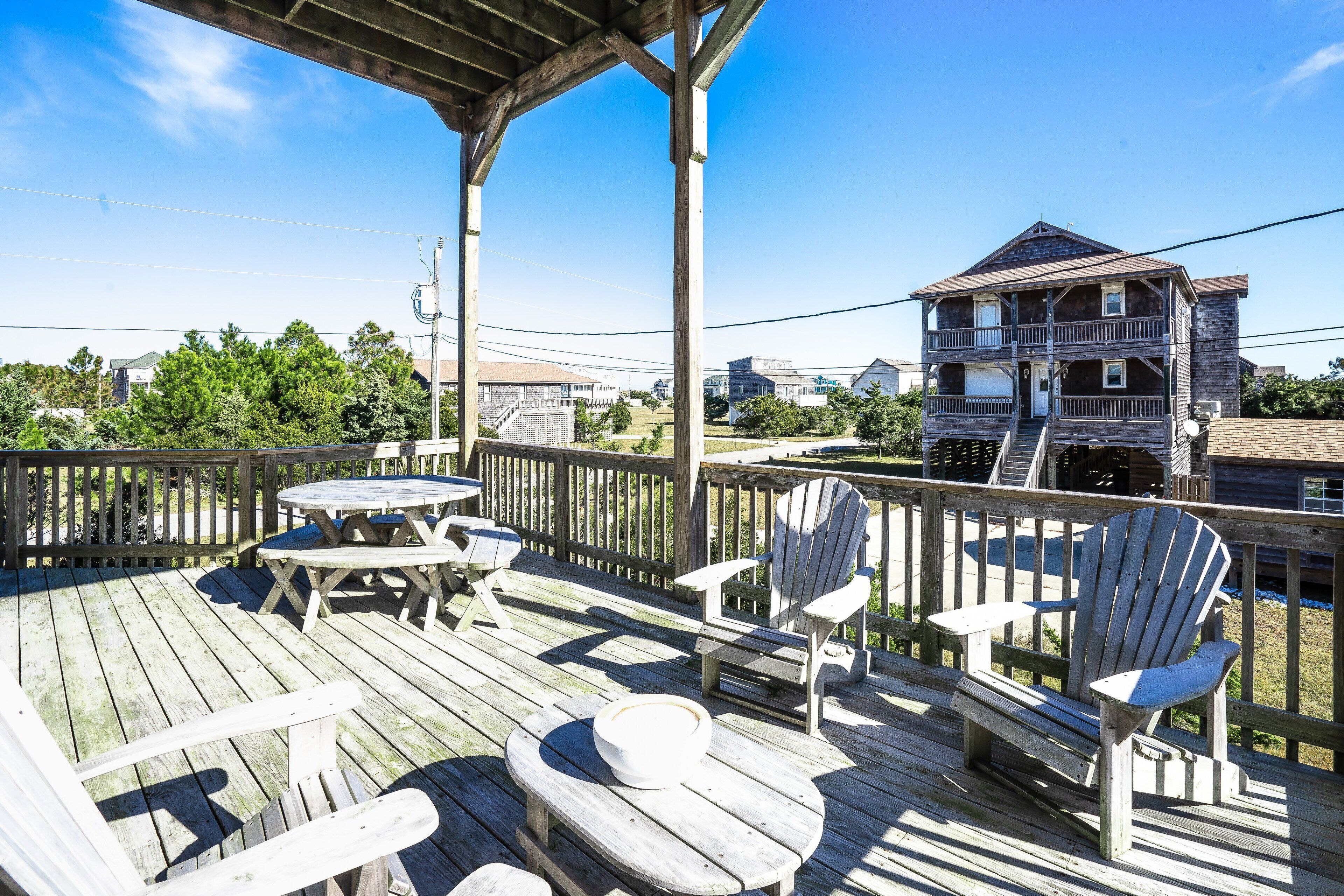 A wooden deck with outdoor seating, including tables and chairs, overlooking a residential area with houses.