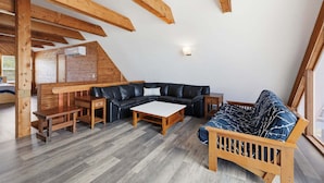 Habitación estilo loft con vigas de madera a la vista, un sofá seccional de cuero negro, una mesa de centro de madera y un banco de madera.