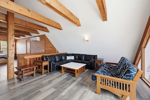 A loft-style room with exposed wooden beams, a black leather sectional sofa, a wooden coffee table, and a wooden bench.
