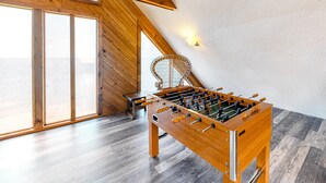 A wooden foosball table in a room with large windows and a sloped ceiling. - Waterfront  house with pool, W/D, private hot tub, & AC (Frisco)