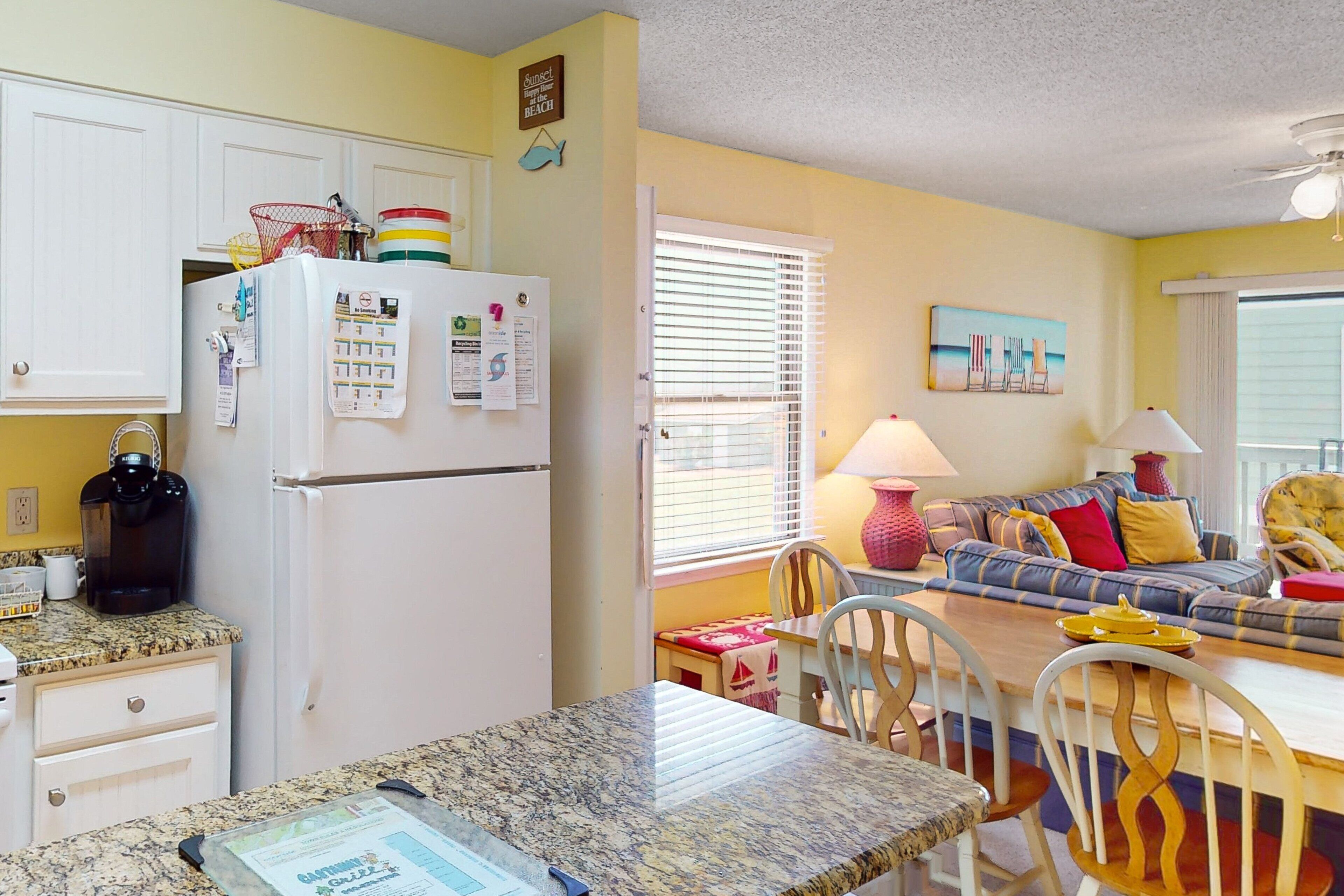 A kitchen with a refrigerator, a coffee maker, and a dining area with a table and chairs.