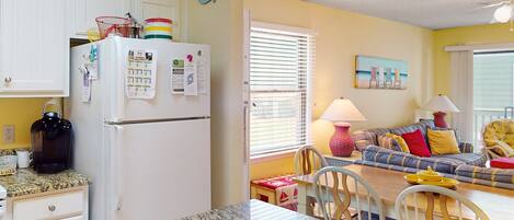 A kitchen with a refrigerator, a coffee maker, and a dining area with a table and chairs.