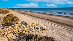 En strand med en træpromenade, der fører hen til en bygning med rødt tag.