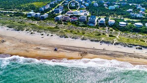Ett flygbildsbild av ett bostadsområde vid kusten med hus, en strand och havet.