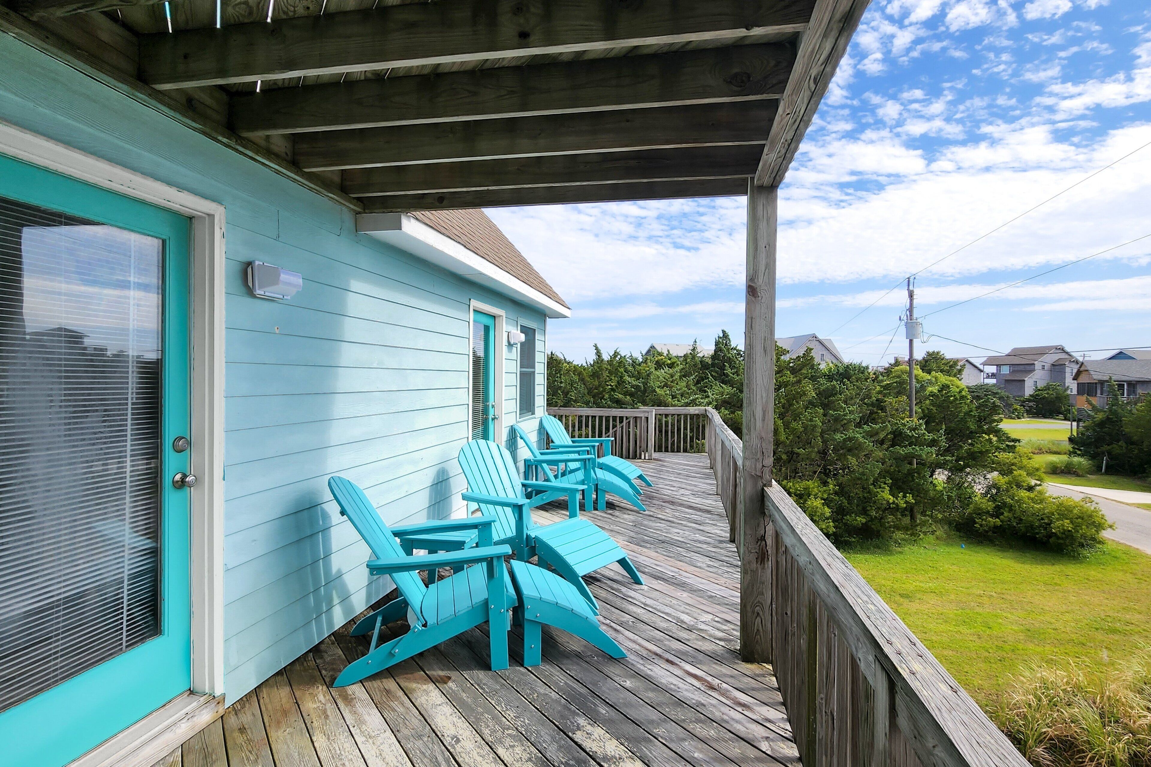 Uma casa turquesa com um deck de madeira e área de estar externa.