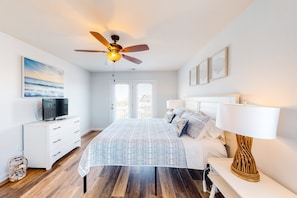 A bedroom with a bed, a ceiling fan, a TV on a dresser, and a view of the outside.