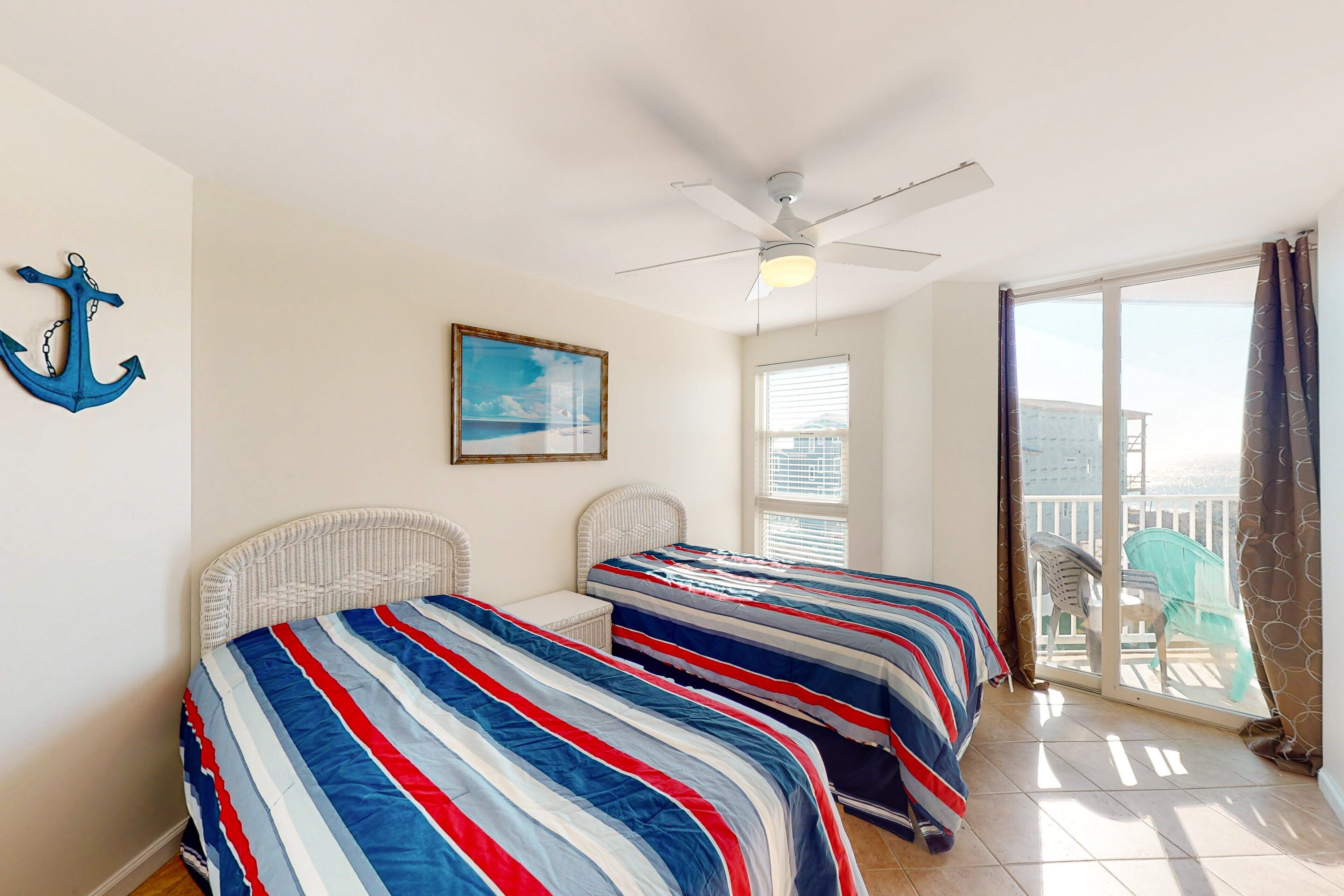 A room with two beds, a ceiling fan, a painting, and a view of the outdoors.