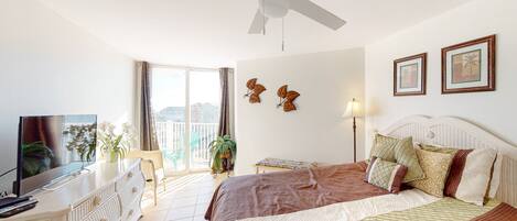 A hotel room with a bed, a television, a desk, and a balcony with plants.