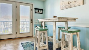 A room with a wooden table and stools, a blue rug, and a painting on the wall.
