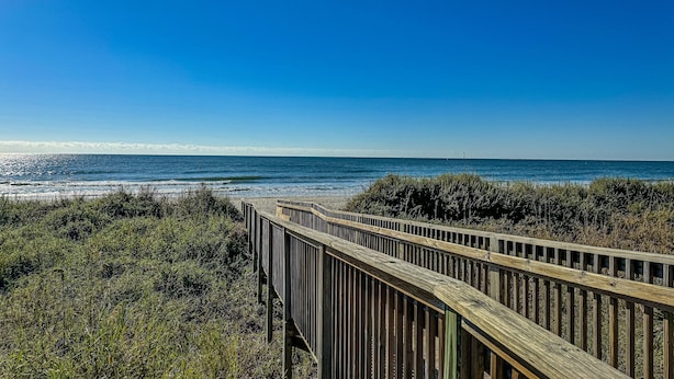 A wooden boardwalk leading to a beach with clear skies.