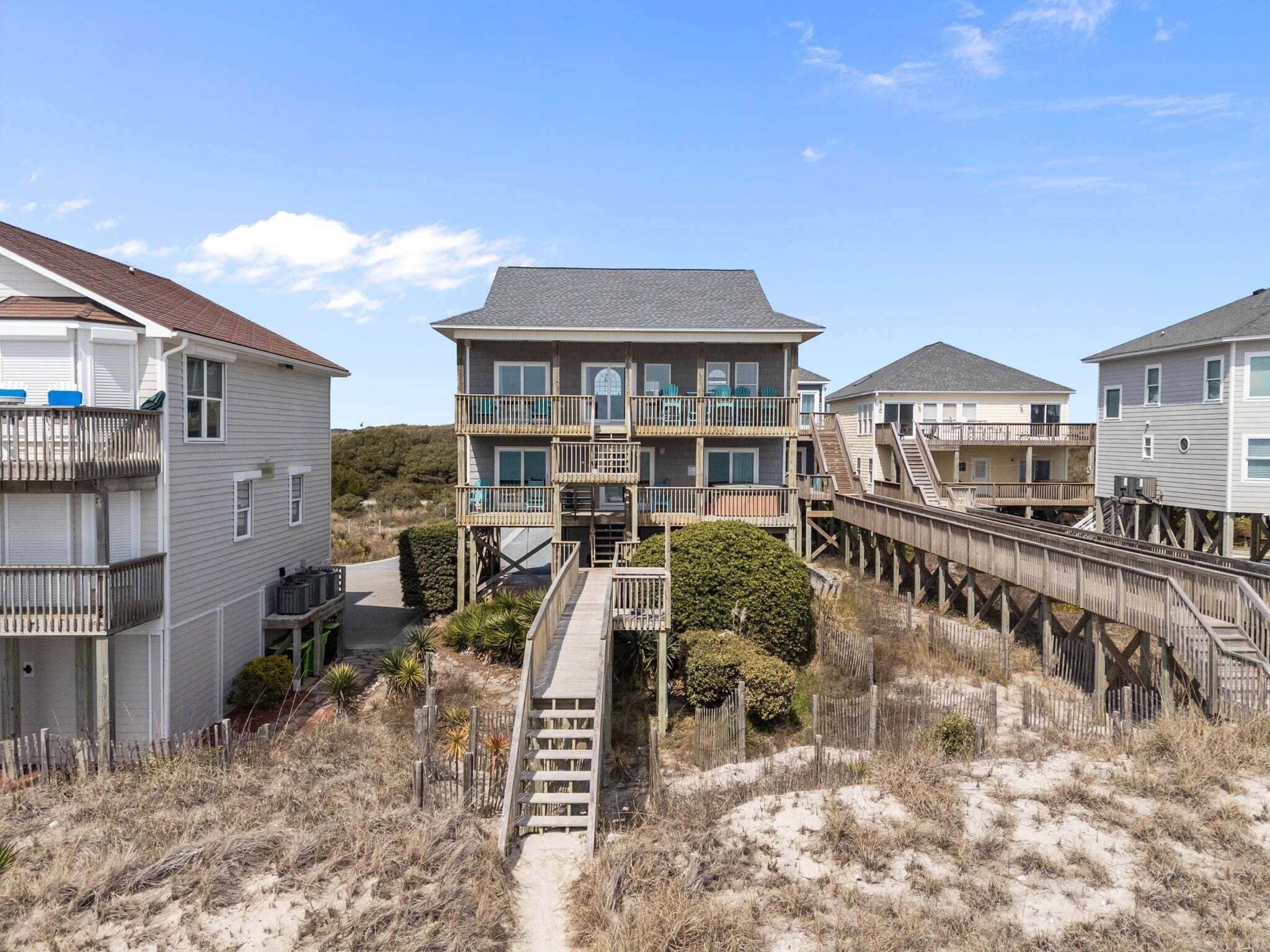 A beachfront property with a central building featuring a balcony and a wooden walkway leading to it.