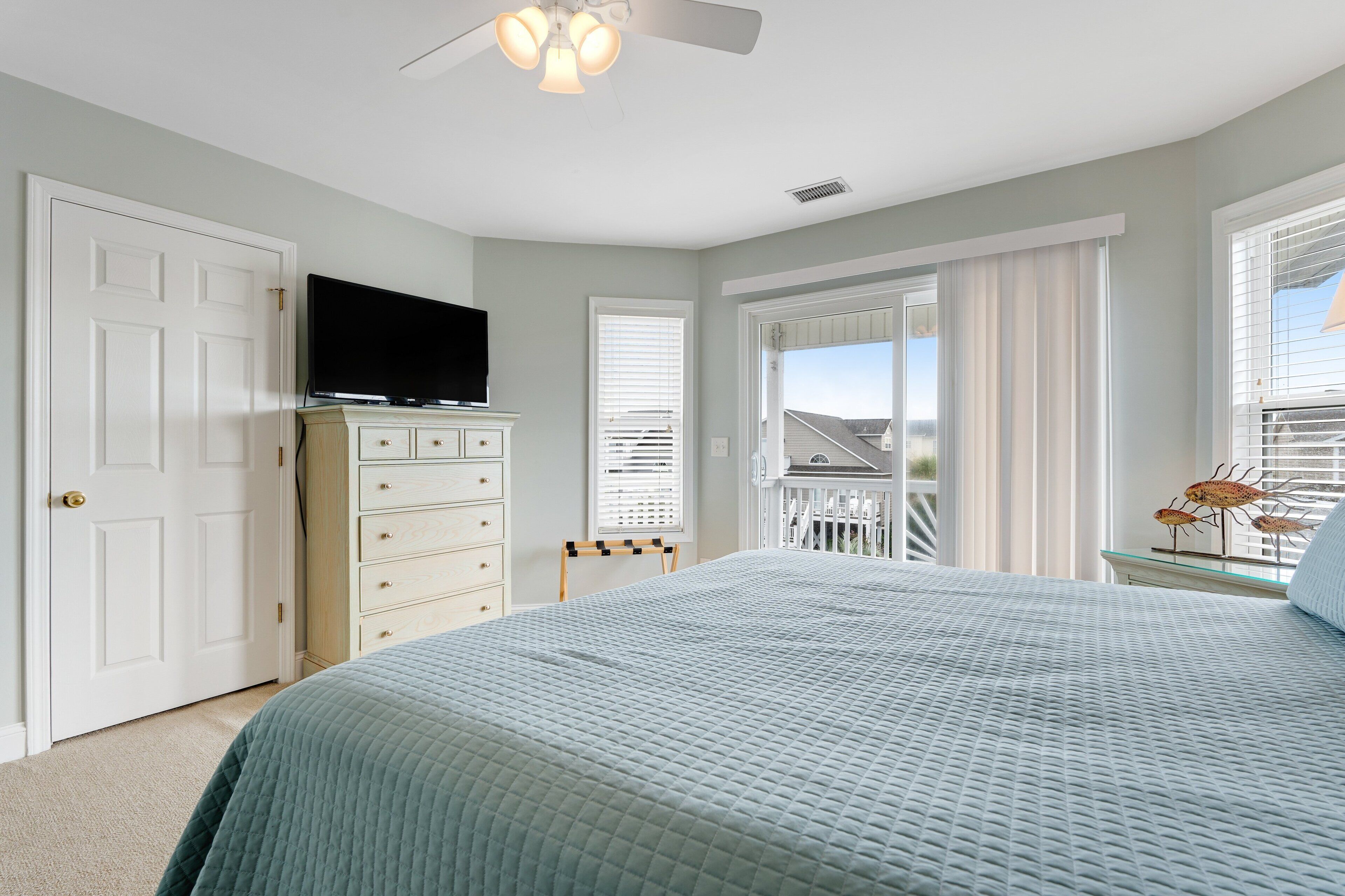 A bedroom with a bed, a TV on a dresser, a ceiling fan, and a balcony with a railing.