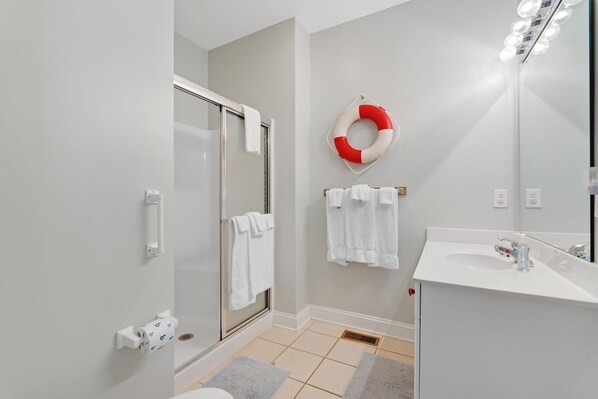Une salle de bain moderne avec une douche en verre, un lavabo blanc et une bouée rouge et blanche accrochée au mur.