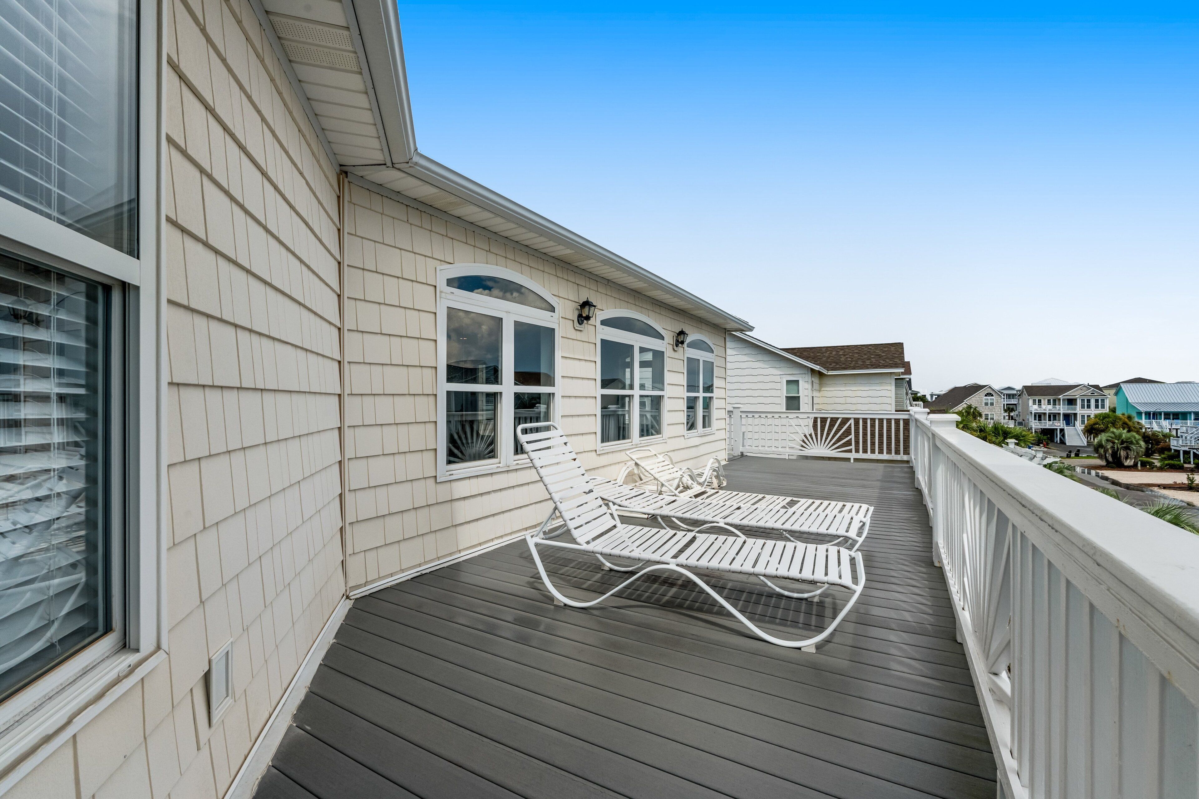 Une terrasse extérieure couverte, dotée de deux chaises longues blanches, d’un plancher en bois et d’une rambarde blanche.