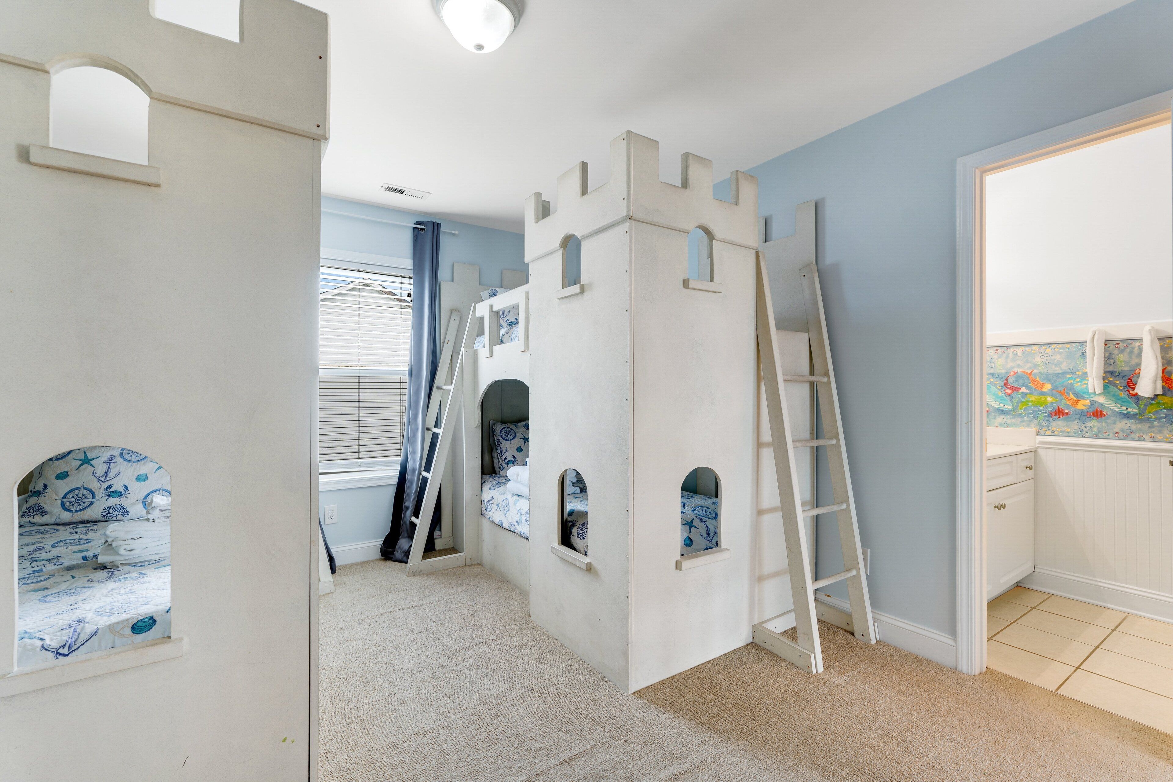 A child's playroom with a castle-themed bunk bed, a ladder, and a window with blinds.
