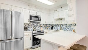 Une cuisine moderne avec des meubles blancs, des appareils en acier inoxydable, un pare-feu en carrelage et un îlot central doté de sièges.