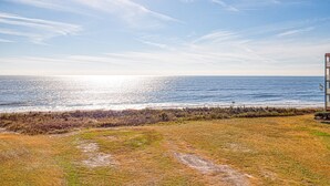 Une vue sur la côte, avec un ciel dégagé, une plage de sable et un bâtiment doté d’un balcon donnant sur l’océan.