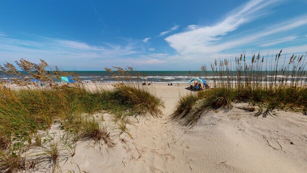 A beach with dunes, a clear sky, and a distant view of the ocean. - Deja Blue: Oceanfront Perfection (Ocean Isle Beach)