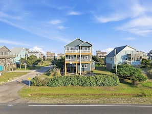 A multi-story residential building with a balcony, surrounded by other houses, a road, and greenery.