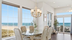A dining area with a glass table and wicker chairs, large windows with a beach view, and a ceiling fan. - Oceanfront, Next door to Pool, Easy Access, Oversized Deck (North Topsail Beach)