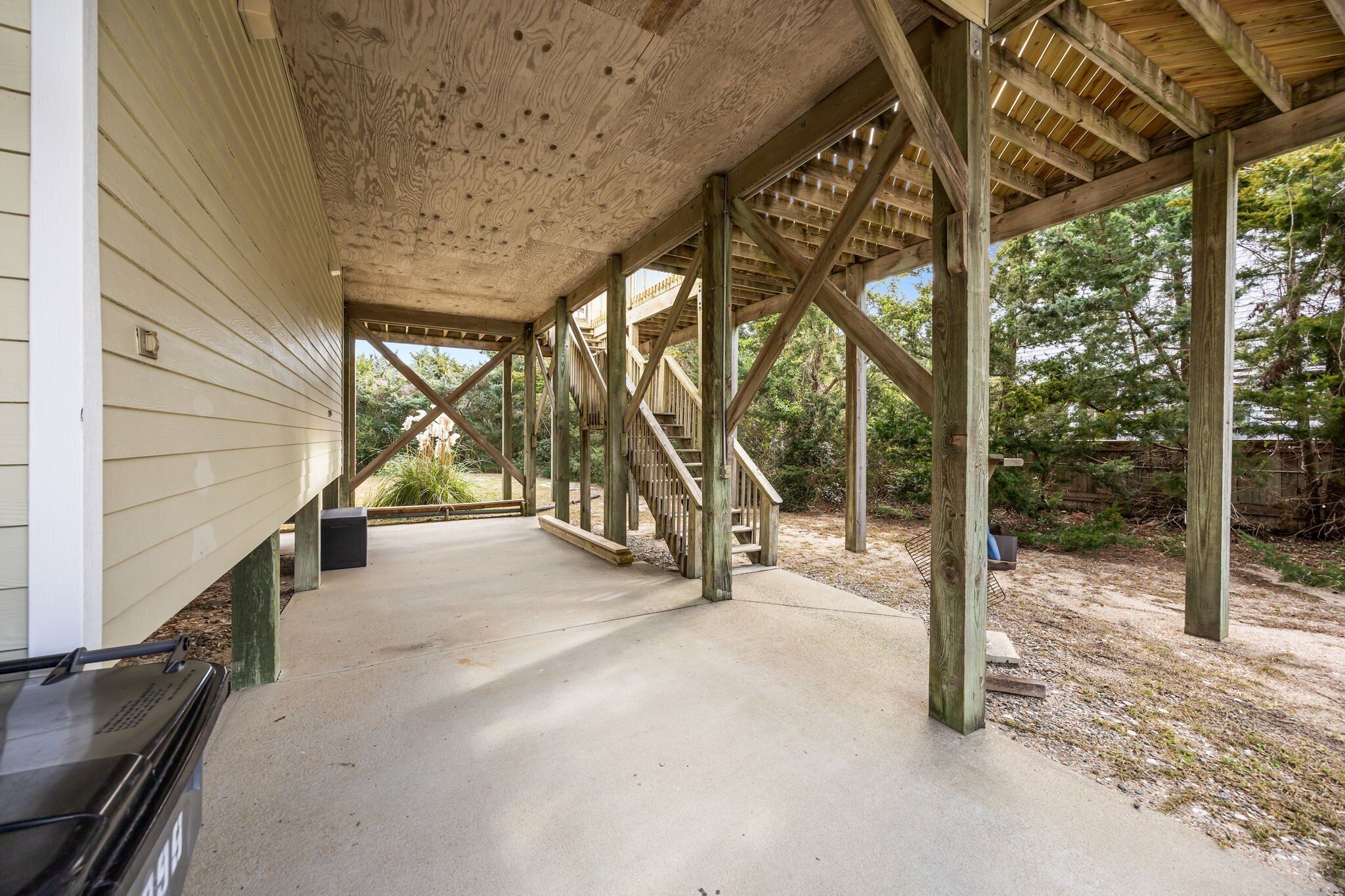 A covered outdoor area with wooden beams and a concrete floor, leading to a staircase.