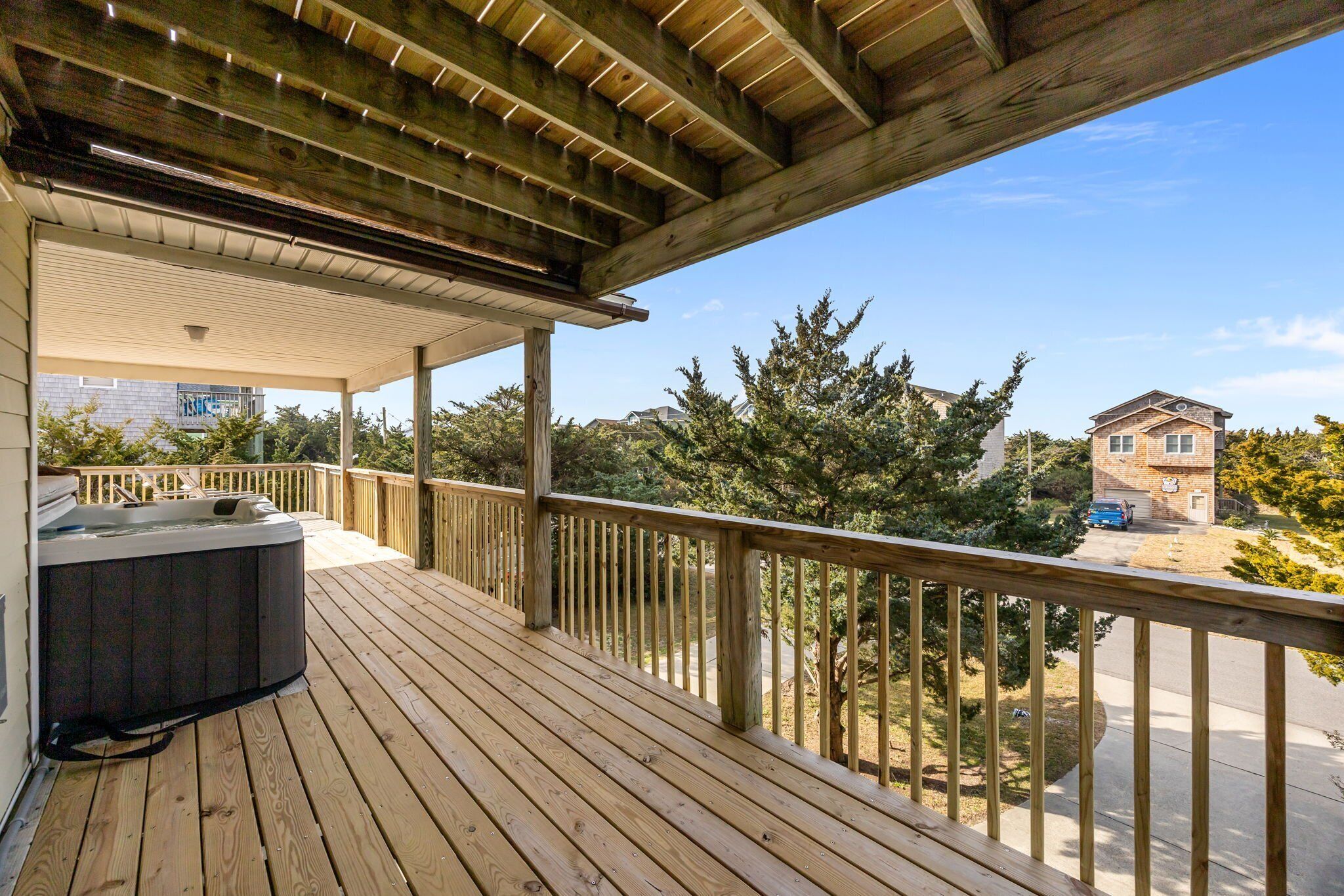 A wooden deck with a hot tub, a covered area, and a view of a residential neighborhood.