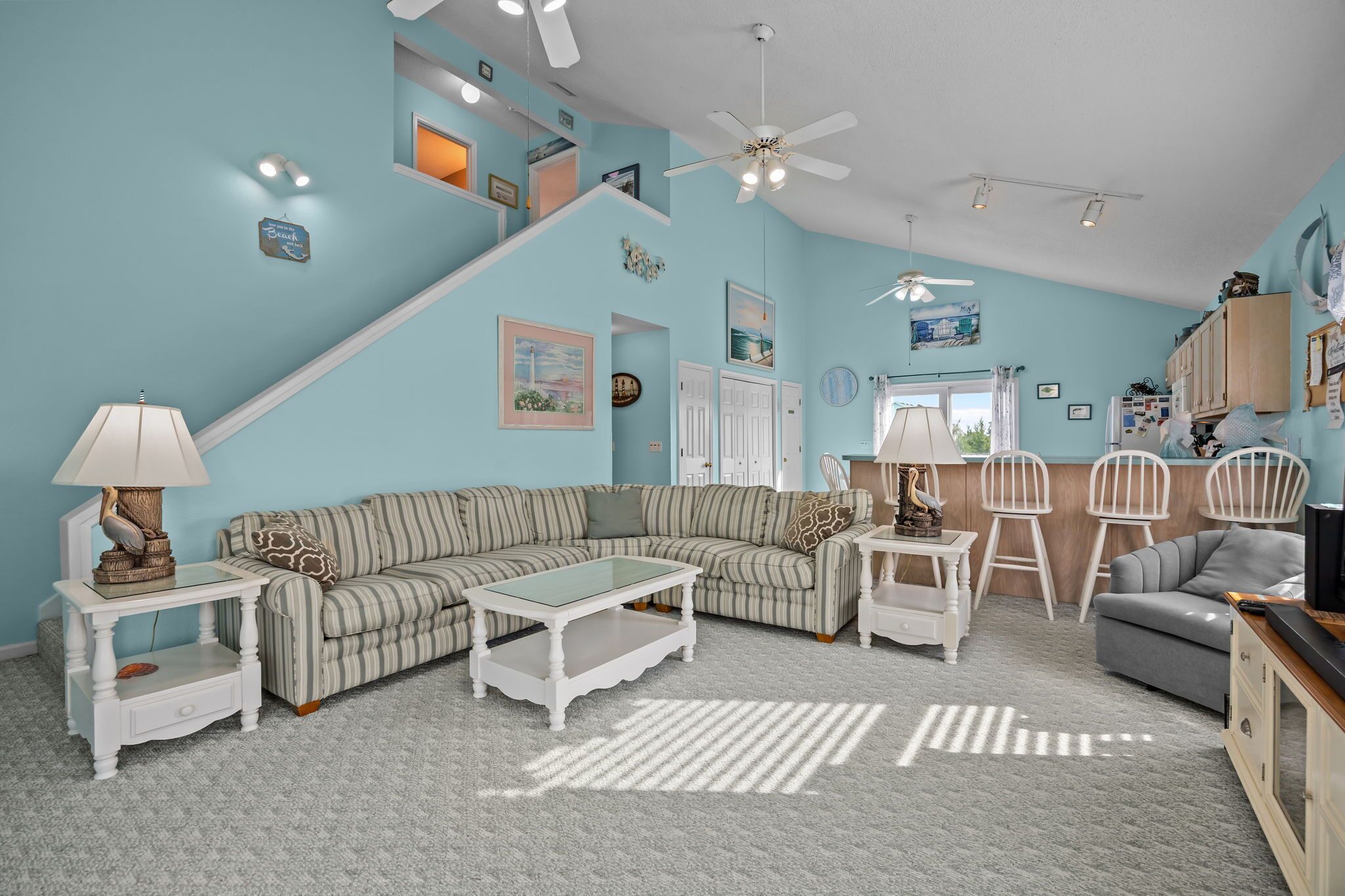 A living room with a striped sofa, a glass coffee table, and a white armchair. There is a staircase leading to an upper level.