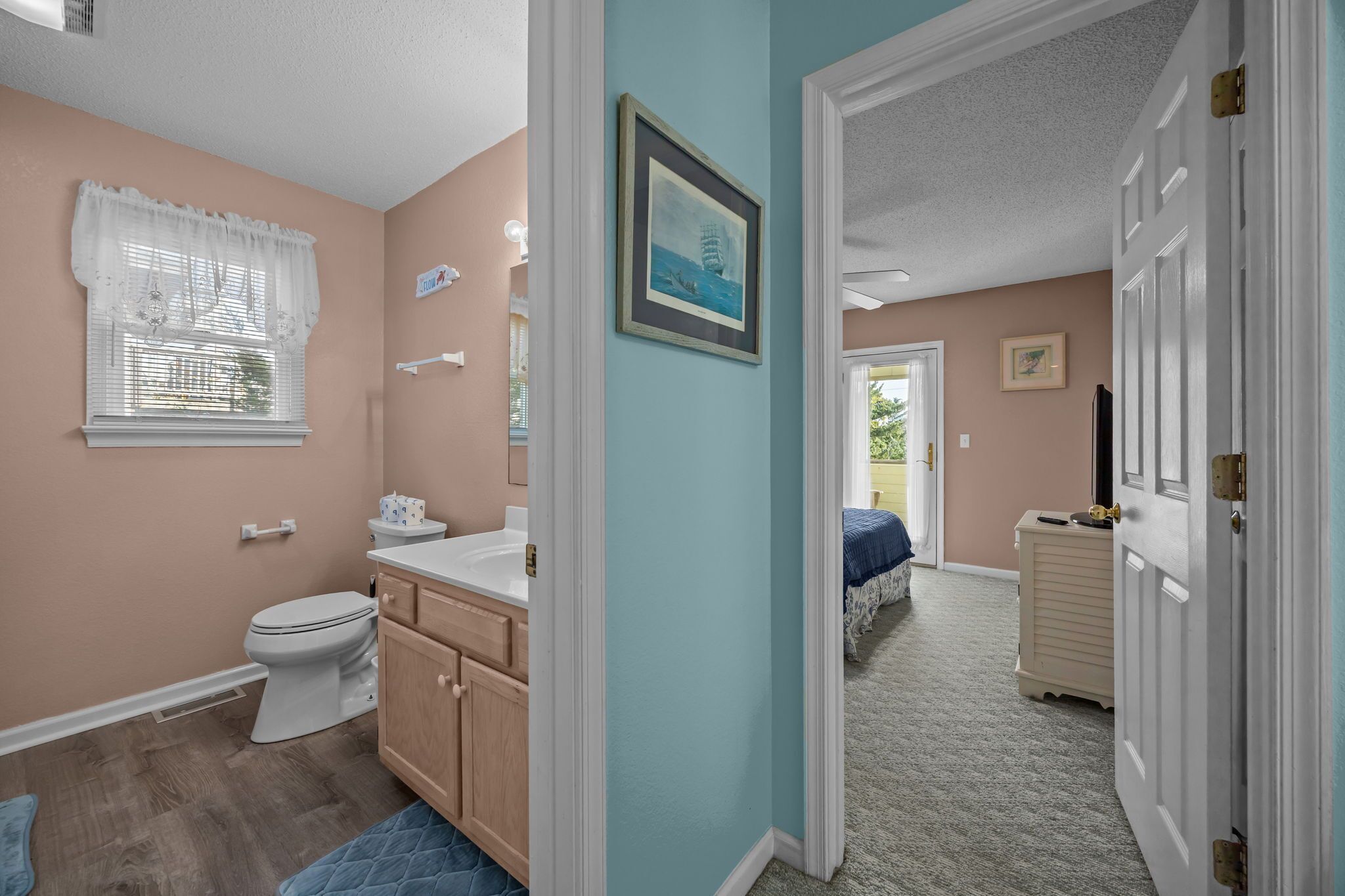 A bathroom with a toilet, vanity, and a window with a white curtain.