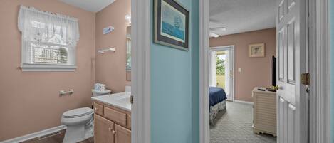 A bathroom with a toilet, vanity, and a window with a white curtain.